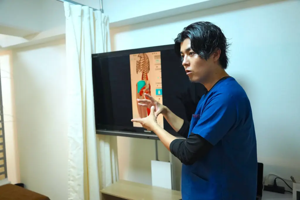 モニターに表示した背骨と筋肉の図を指しながら施術内容を説明する様子