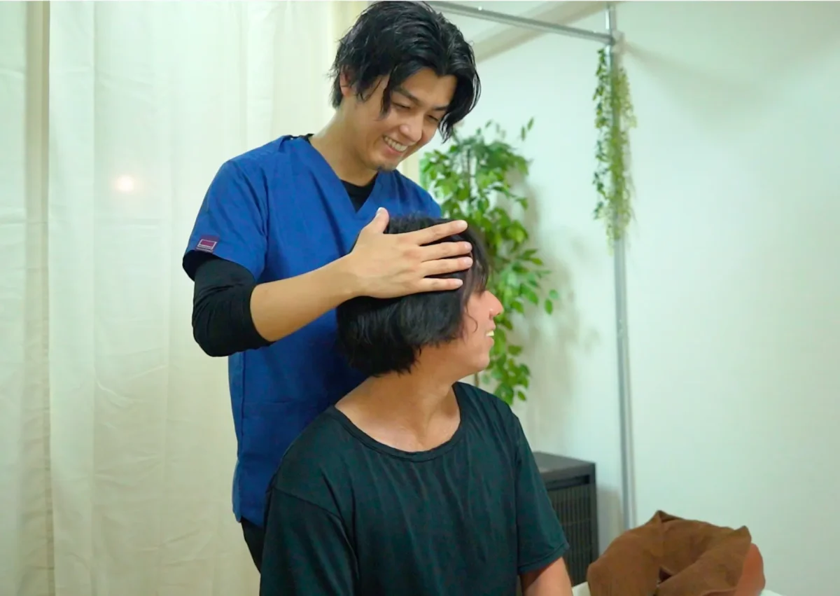 六本木の整体サロン「モビリティ整体ソシオ」で、整体師がお客様の首や頭部の可動域を丁寧に検査している様子。姿勢や動きのクセを確認するシーン。