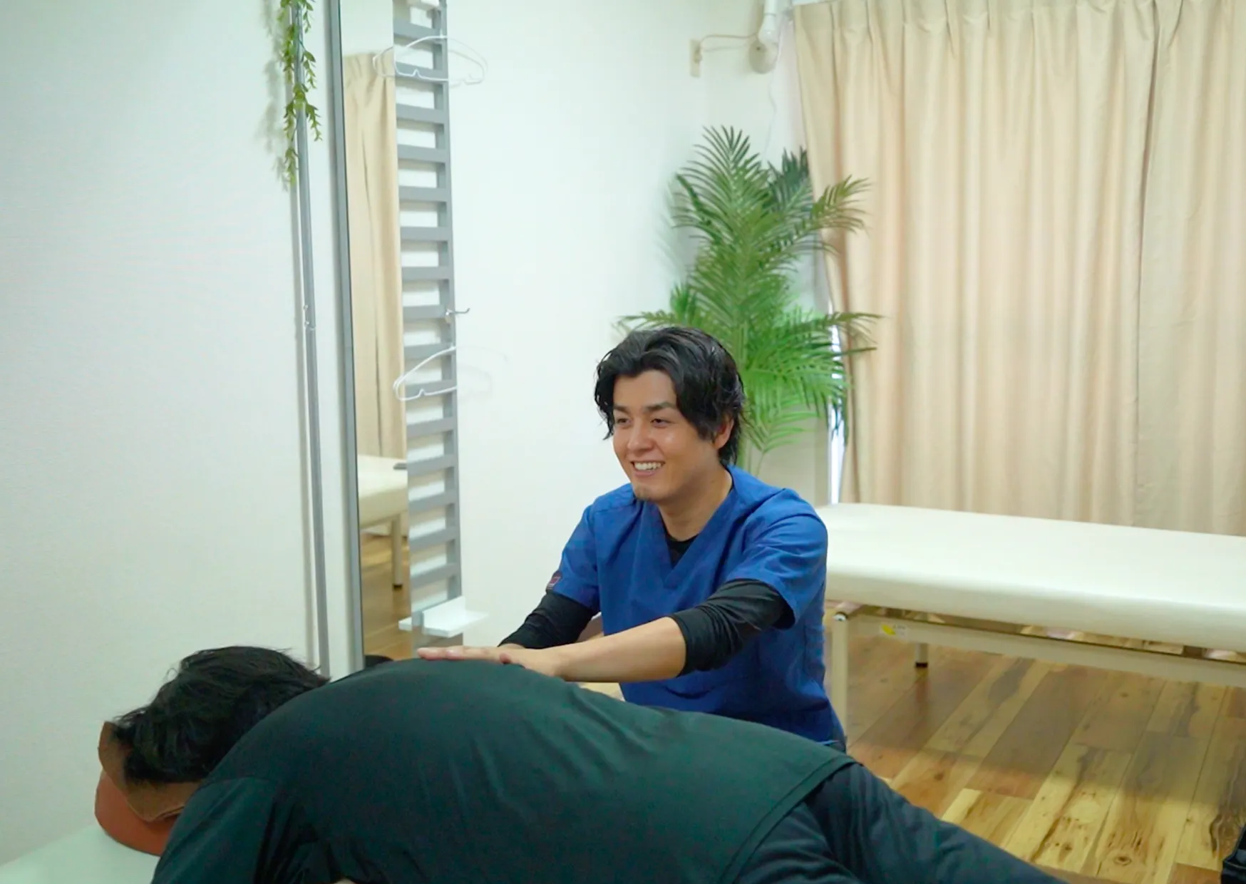 六本木の整体でうつ伏せの患者様の背中に両手を当てて施術する柔道整復師